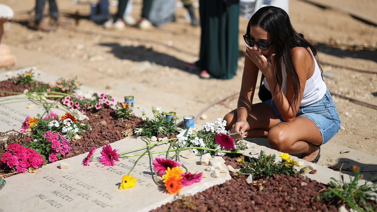 Mulher se ajoelha ao lado de um memorial