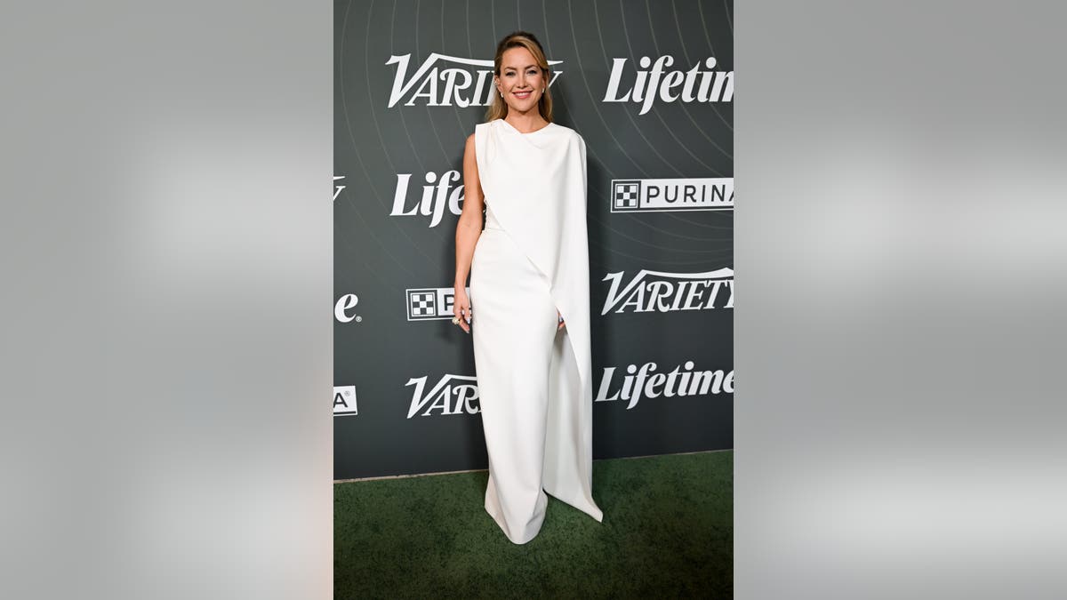 Kate Hudson poses on the red carpet in a white asymmetrical gown at Variety’s 2025 Power of Women Los Angeles event.