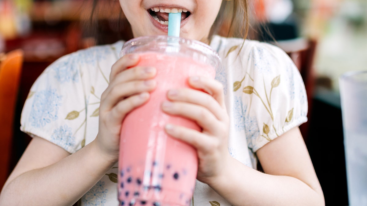 Gadis kecil minum teh gelembung merah muda dari sedotan biru