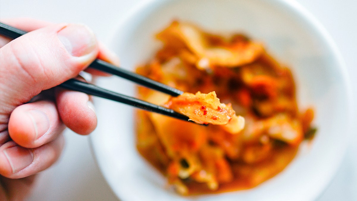 Hands holding kimchi with chopsticks