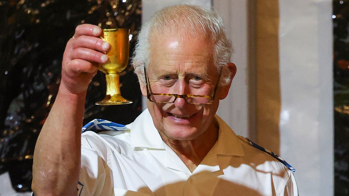 King Charles making a toast while holding a golden cup.