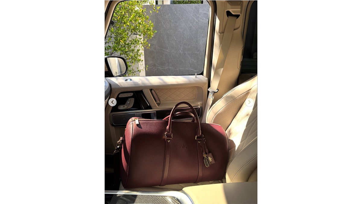 A burgundy Alo duffel bag sits on the front passenger seat of a beige car interior.