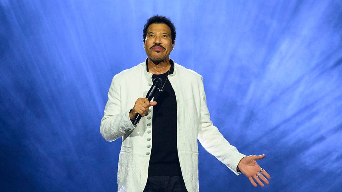 Lionel Richie performs on stage against a blue background with lights.