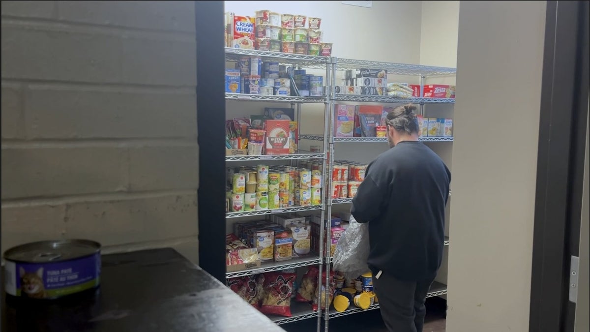 man reaches for a paper bag on a high pantry shelf surrounded by canned goods