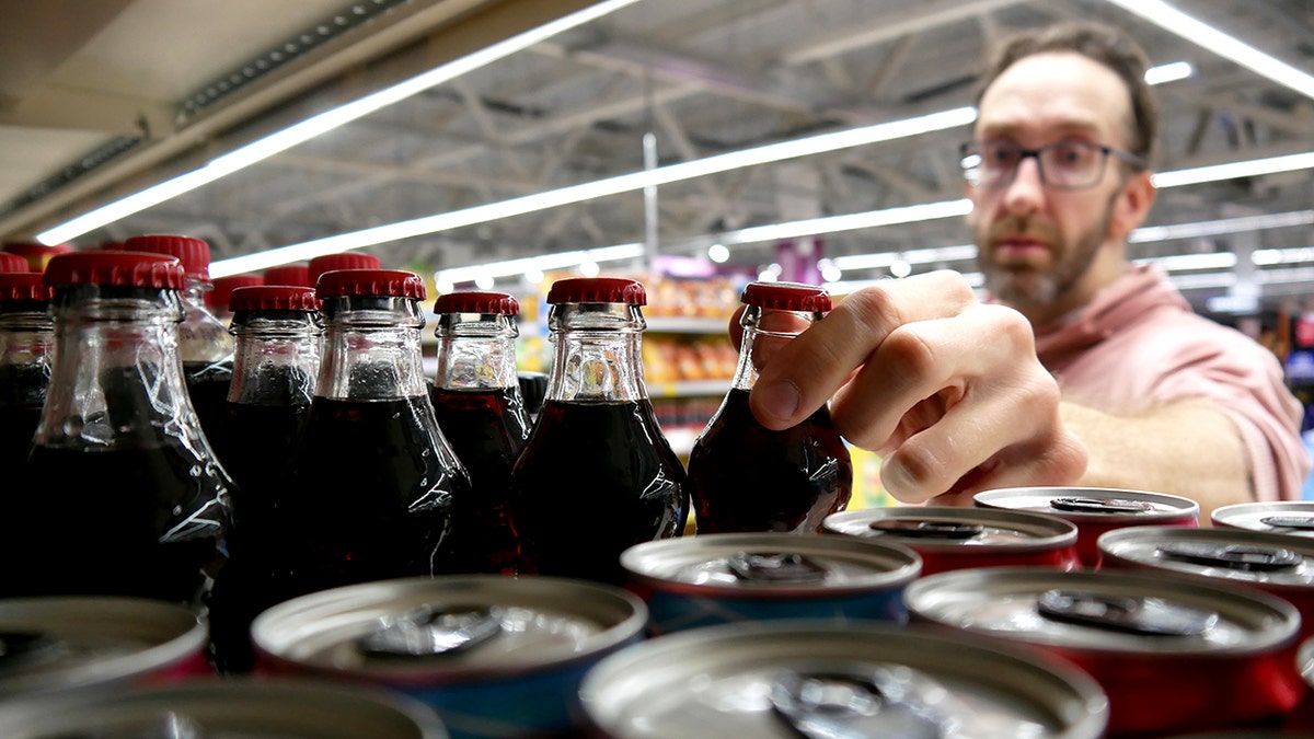 Close-up of a male customer's hand taking a glass bottle of cola