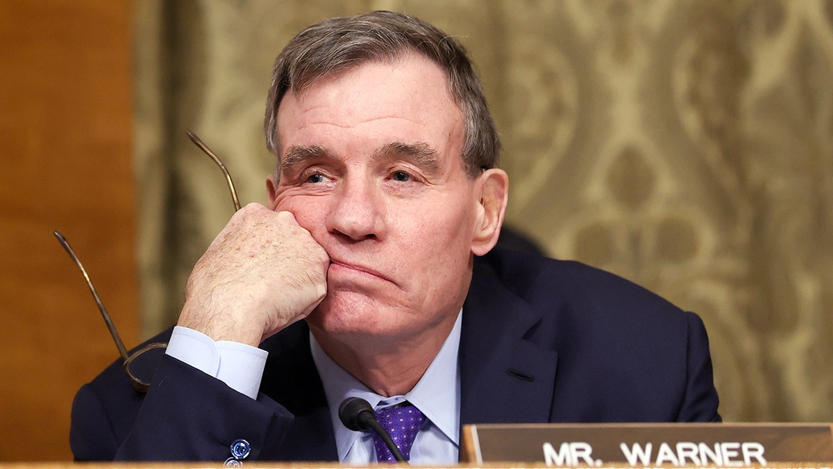 Mark Warner holds his glasses askew at a hearing