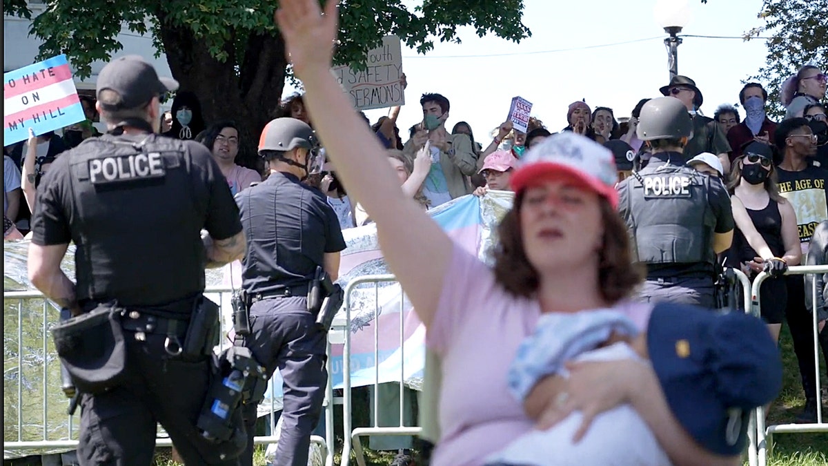 woman with baby worshipping while police block counterprotesters behind her