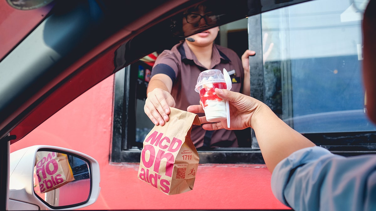 Customer in car receiving hamburger in a bag and ice cream from McDonald's drive thru employee.