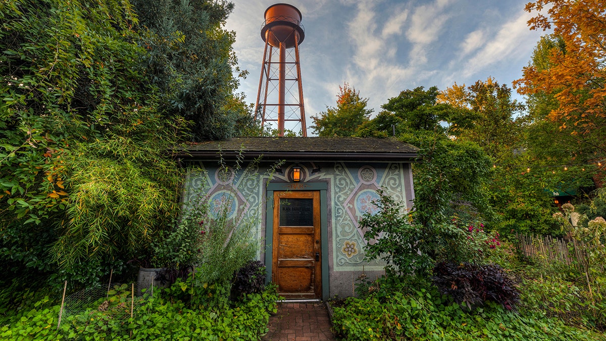 The Black Rabbit House restaurant on the Mcmenamins Edgefield property in Troutdale, Oregon seen surrounded by greenery with water tower in the back.
