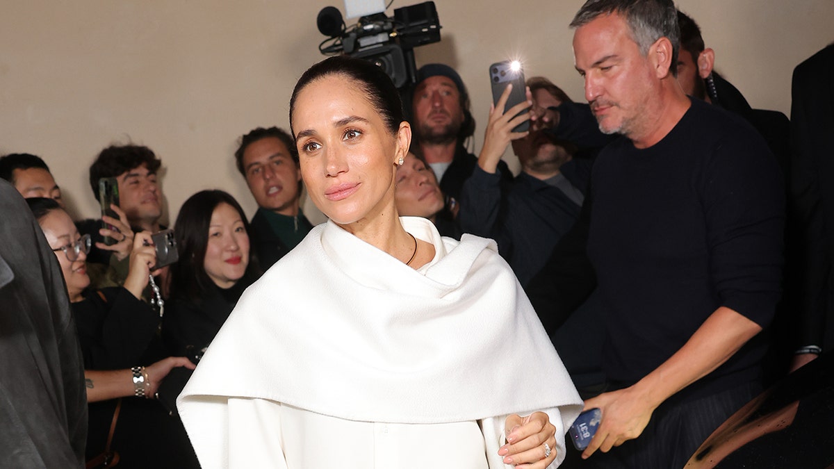 Meghan Markle wearing white while walking in front of photographers.