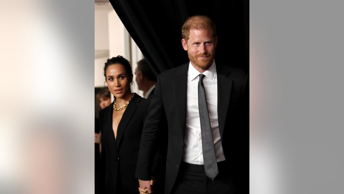 Prince Harry and Meghan Markle in matching formal dark suits, walking together at a gala.