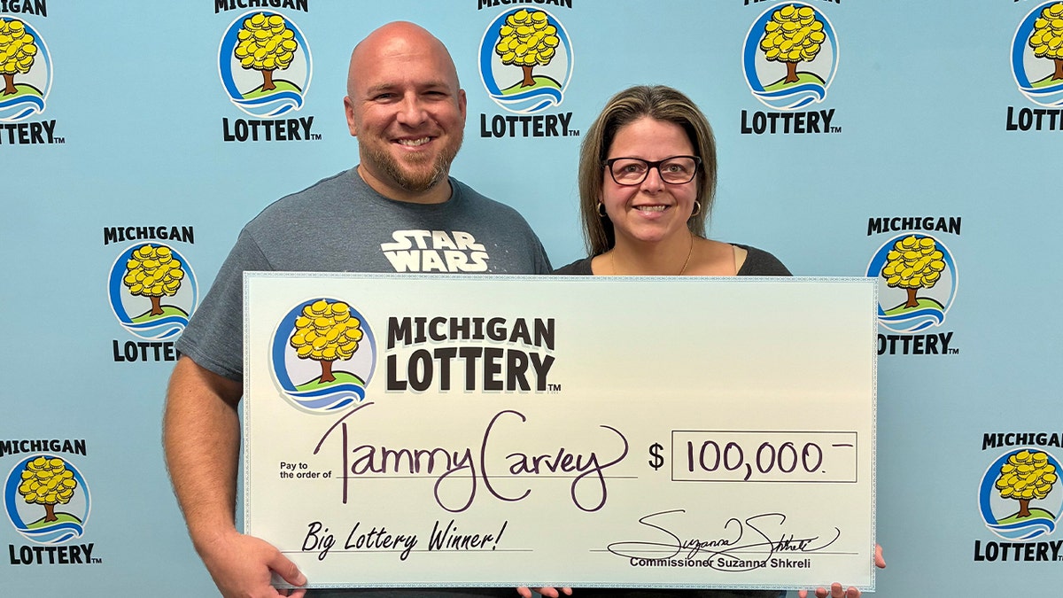 woman stands next to husband with large $100,000 check