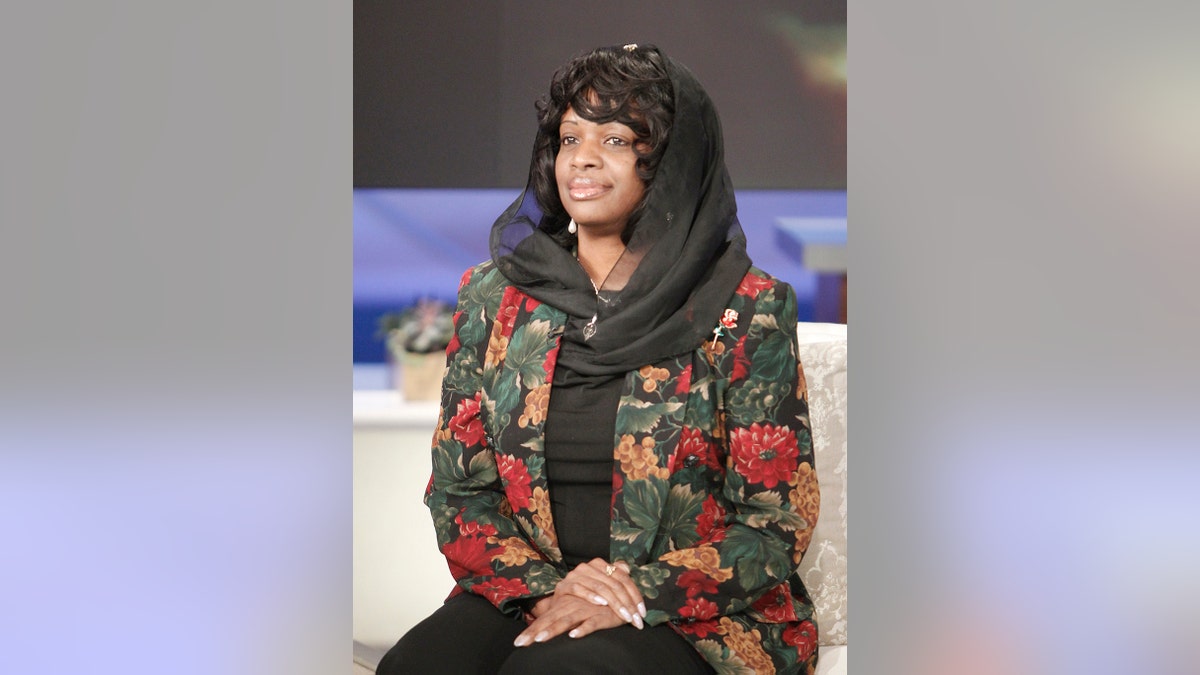 Mildred Muhammad mengenakan setelan merah muda dan tampak tenang, duduk di sofa putih.