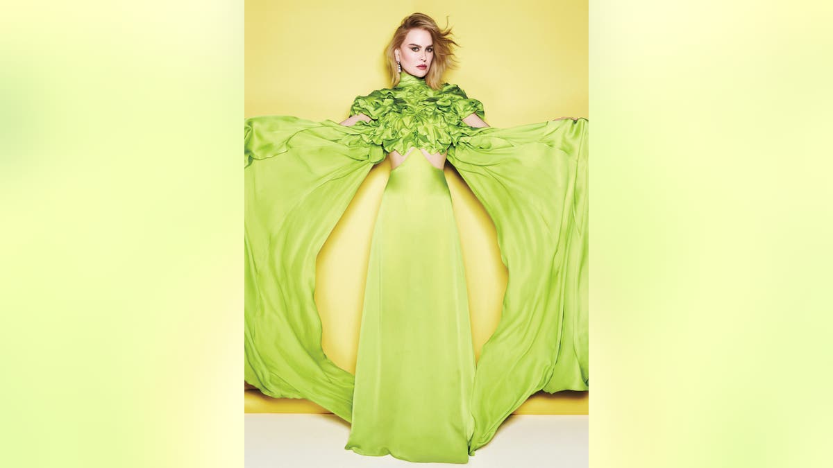 妮可·基德曼 (Nicole Kidman) 身著亮綠色長裙,袖子飄逸,在黃色背景下張開雙臂。