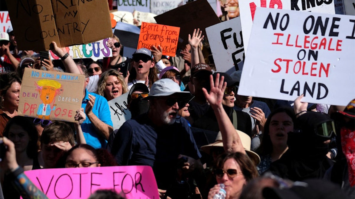 Demonstrators at a No Kings rally hold up signs against the Trump administration