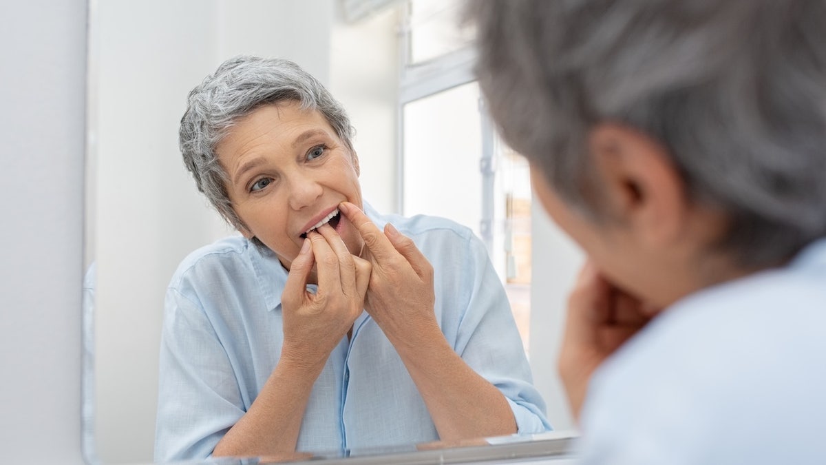 Older woman flossing in bathroom mirror