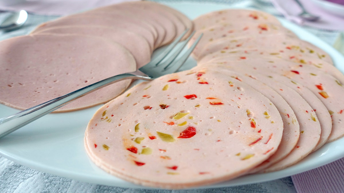 Slices of bologna and olive loaf seen spread out on a plate with a fork