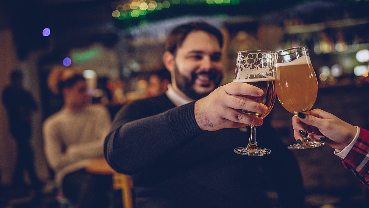 Overweight man clinking beer glass with partner's in a bar.