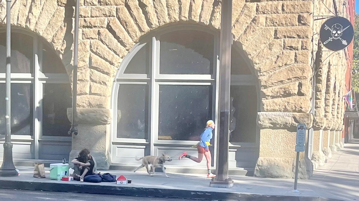 Jogger wikth dog runs past homeless person in Portland, Oregon.