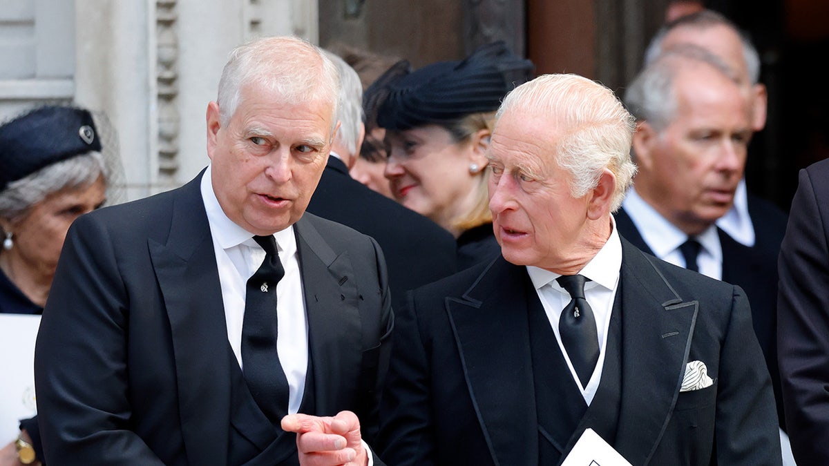 King Charles and the former Prince Andrew in dark suits speaking outdoors.