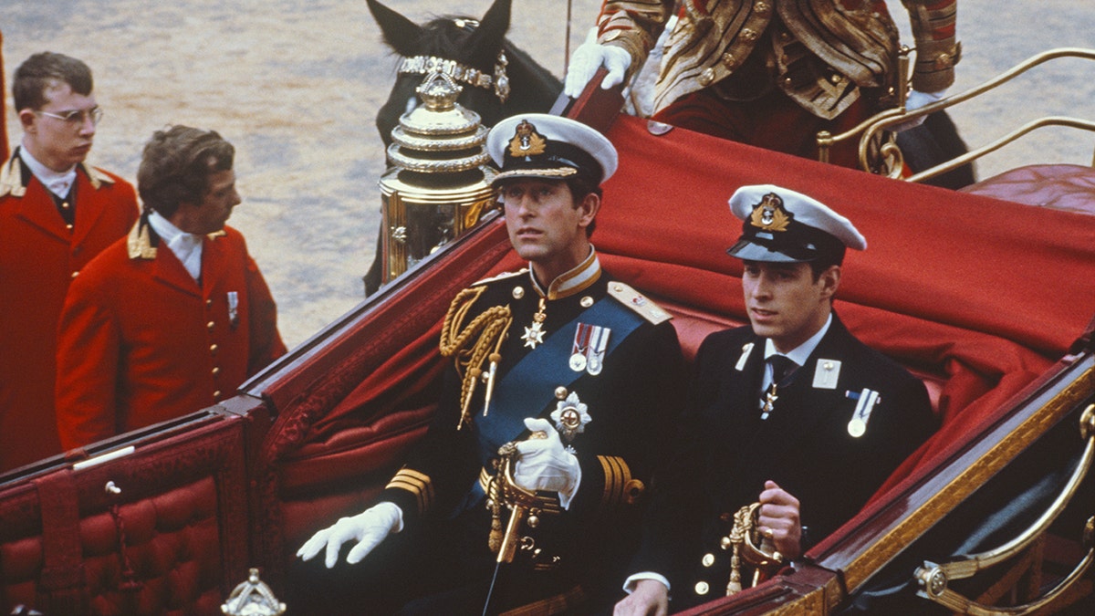 Prince Charles and Prince Andrew in matching military wear sitting in a royal carriage.