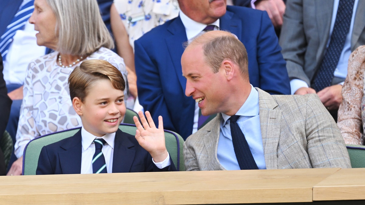 Prince William and his son Prince George smiling at each other while watching a game.