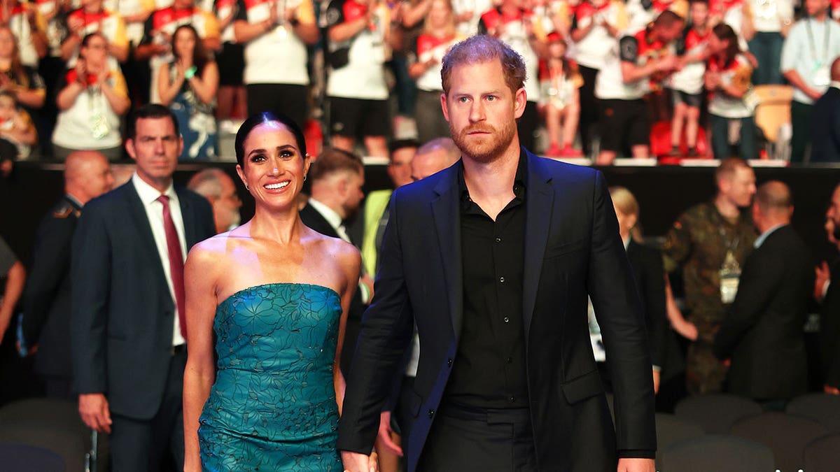 Meghan Markle and Prince Harry holding hands and walking together as a crowd cheers behind them.