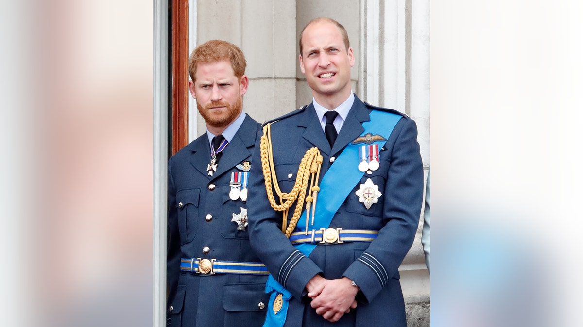 Prince William and Prince Harry in matching uniforms standing on the balcony of Buckingham Palace.