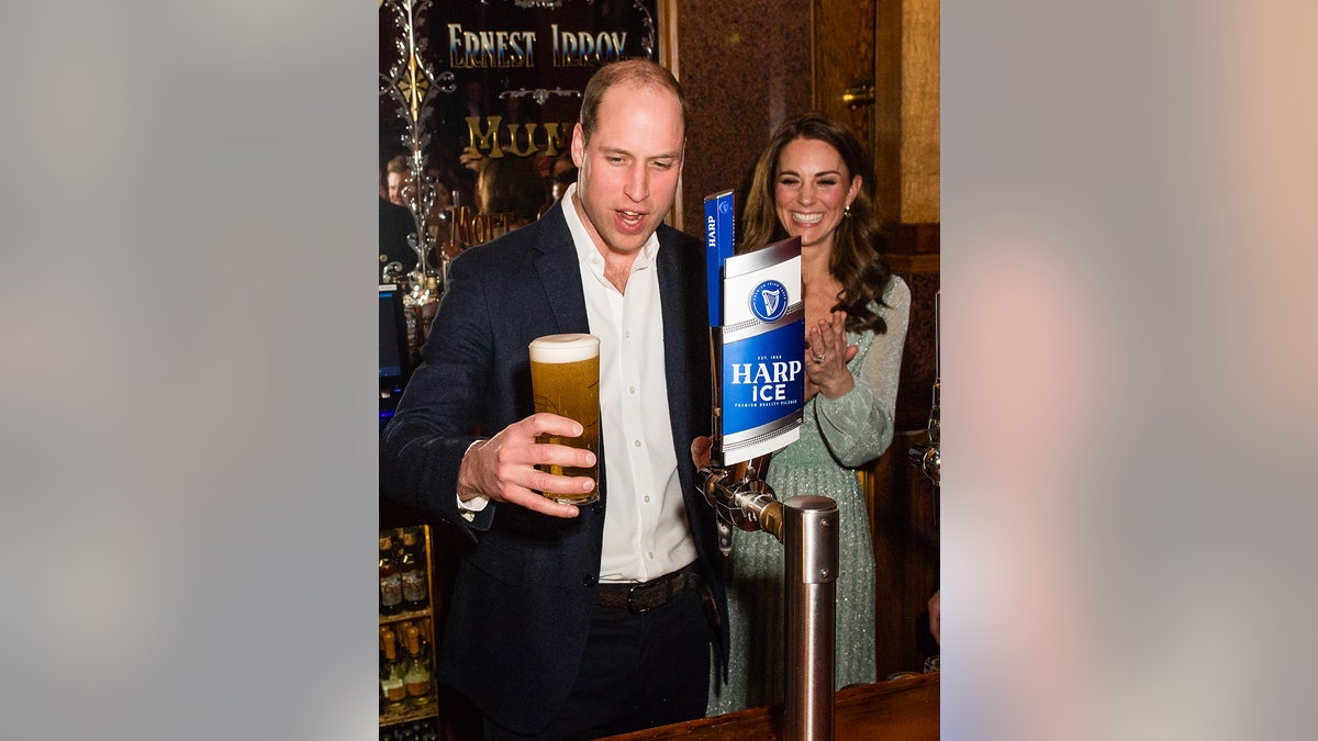Prince William holding a pint of beer while Kate Middleton smiles with glee.