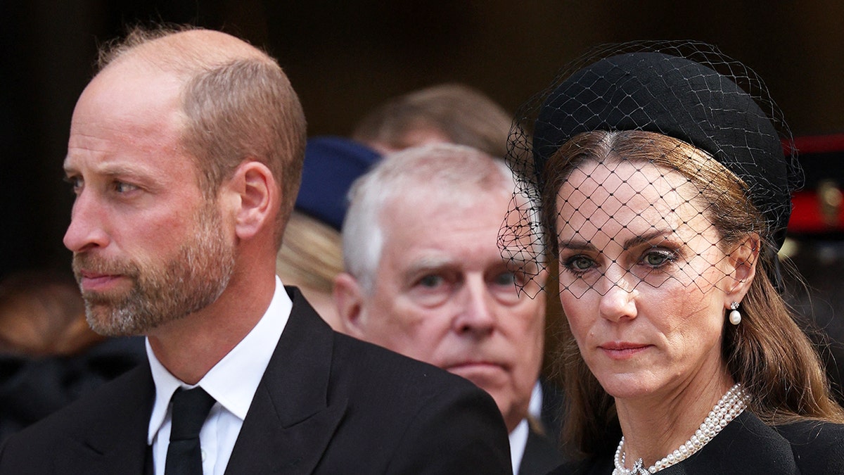 A close-up of Prince William and Kate Middleton looking ahead with Prince Andrew behind them.