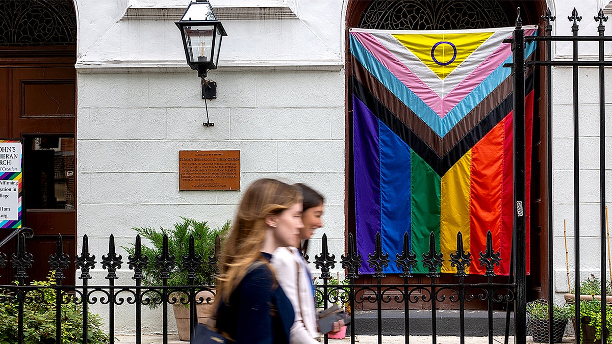 Progress Pride flag hanging outside church as people walk by