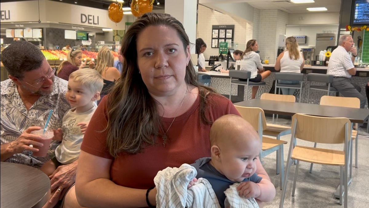 A woman stares at the camera as she sits with her child inside a Publix.