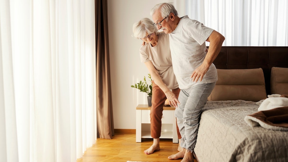 Older woman helping husband stand up - Huntington's disease