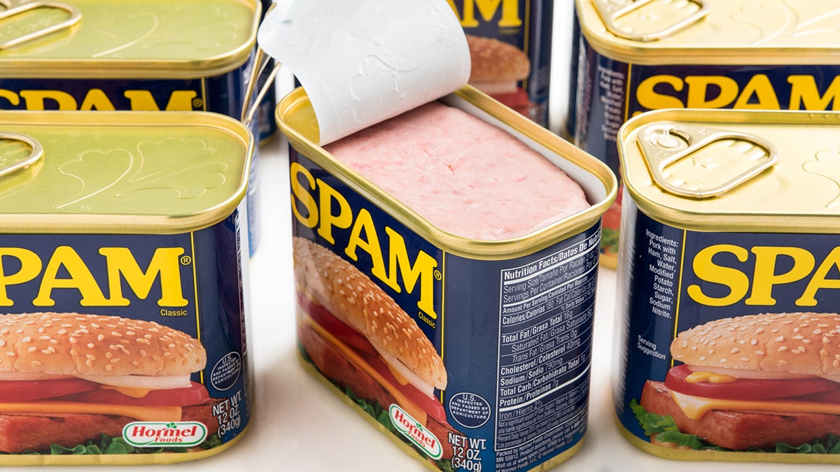 Multiple cans of Spam meat, with one can pried open showing pink meat inside