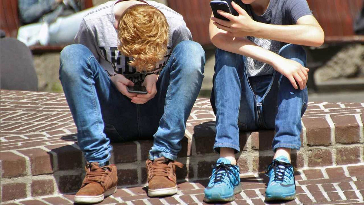 Adolescentes sentados um ao lado do outro em seus telefones