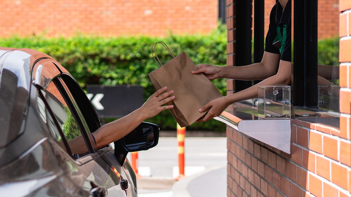 Person in car taking bag from worker at drive-thru restaurant.
