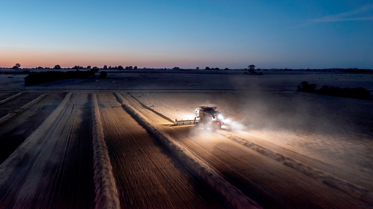 Panoramic aerial landscape view of working combine harvester at night with lights illuminating the field