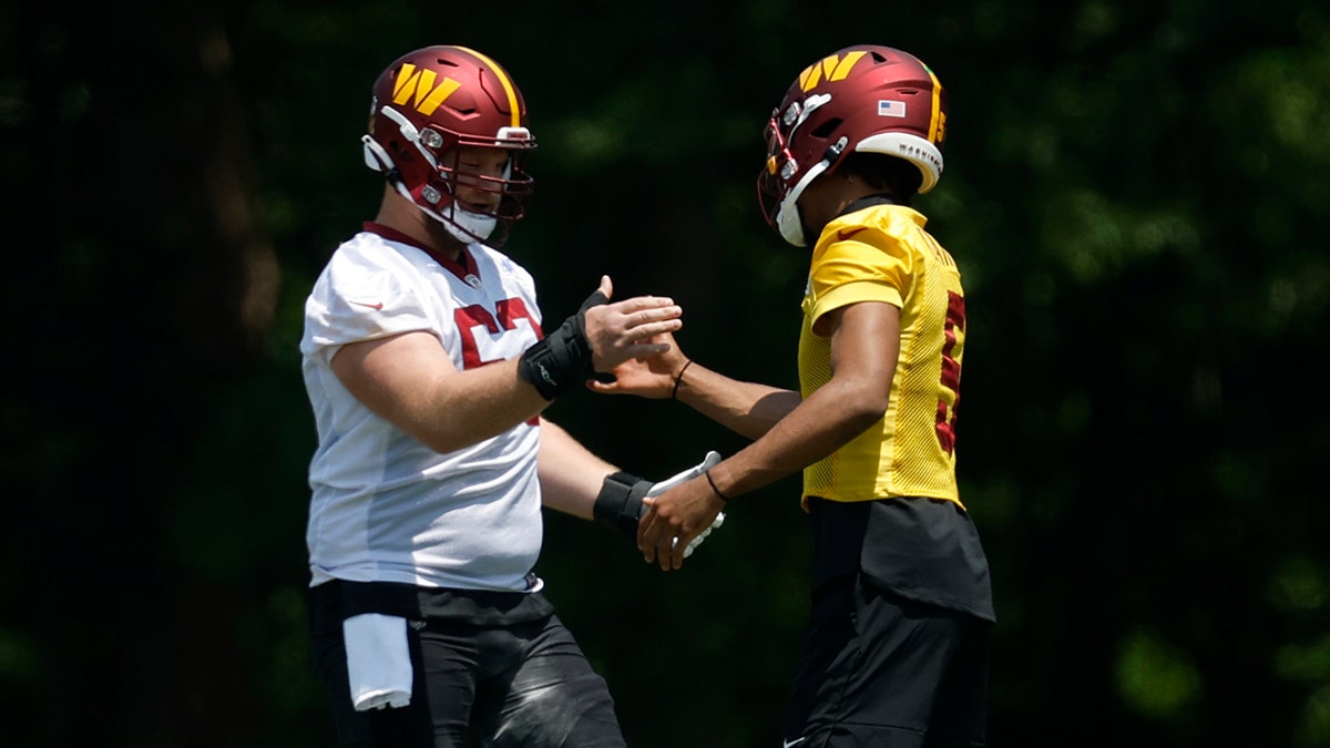 Washington Commanders center Tyler Biadasz (63) shakes hands with Commanders quarterback Jayden Daniels (5) during drills on day one of minicamp at Commanders Park.