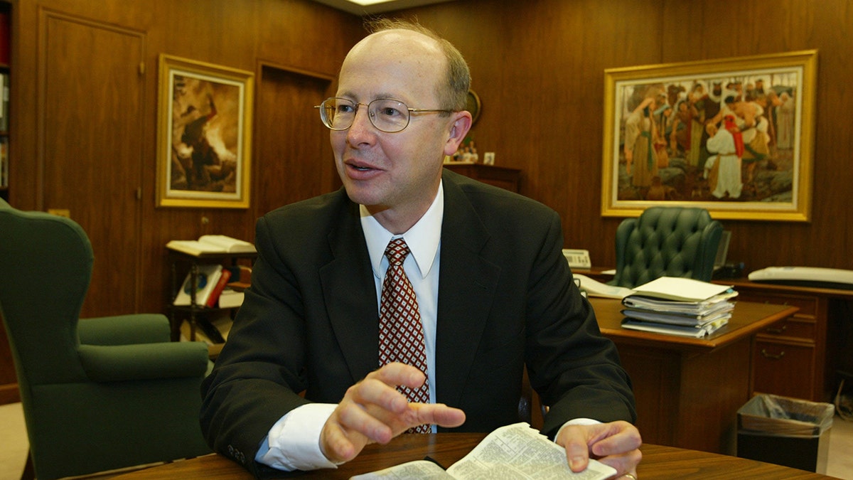 Richard Turley w garniturze przemawiającym, gdy trzyma Biblię.