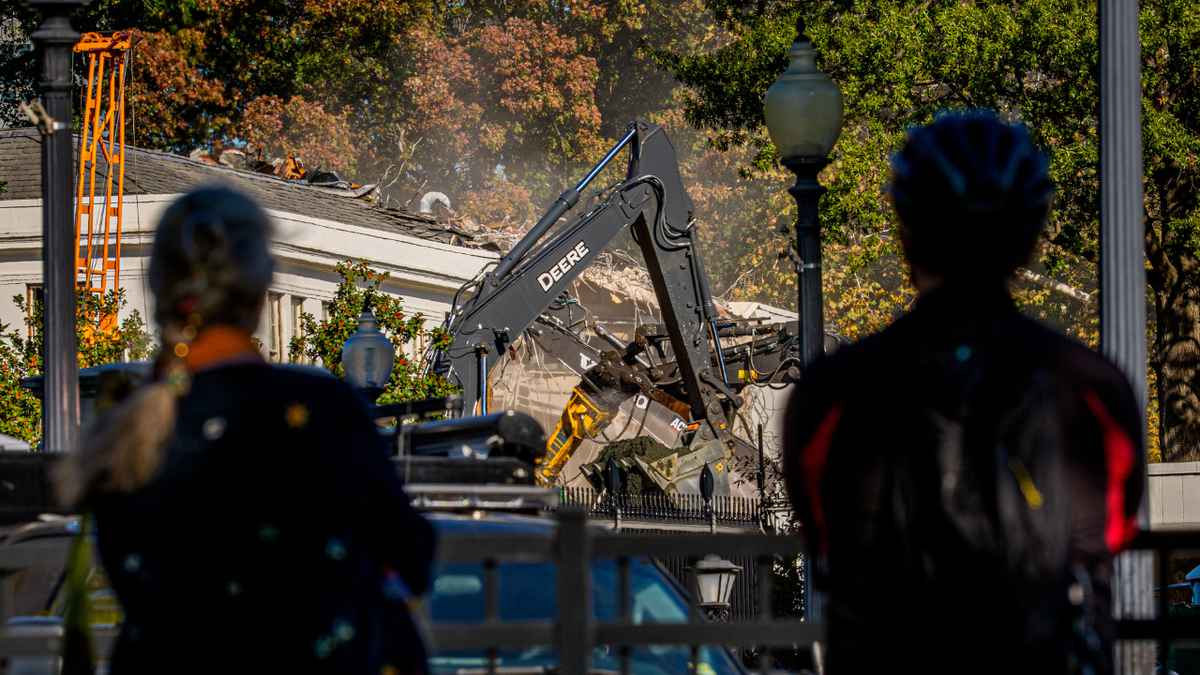 Pedestrians watch the facade of the East Wing of the White House being demolished