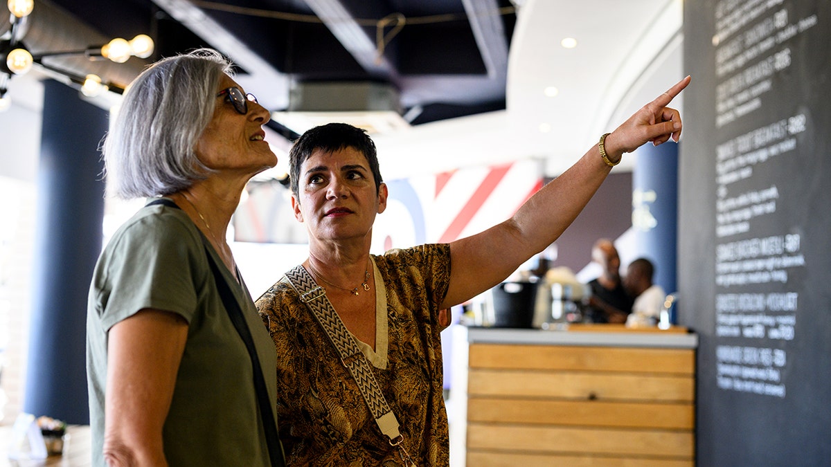 A woman looks at restaurant prices as another woman points.