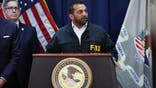 kash patel wears an black FBI jacket while standing at a DOJ podium