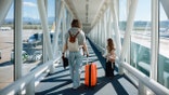 A mother and daughter walking through the jet bridge toward an airplane.