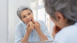Older woman flossing in bathroom mirror