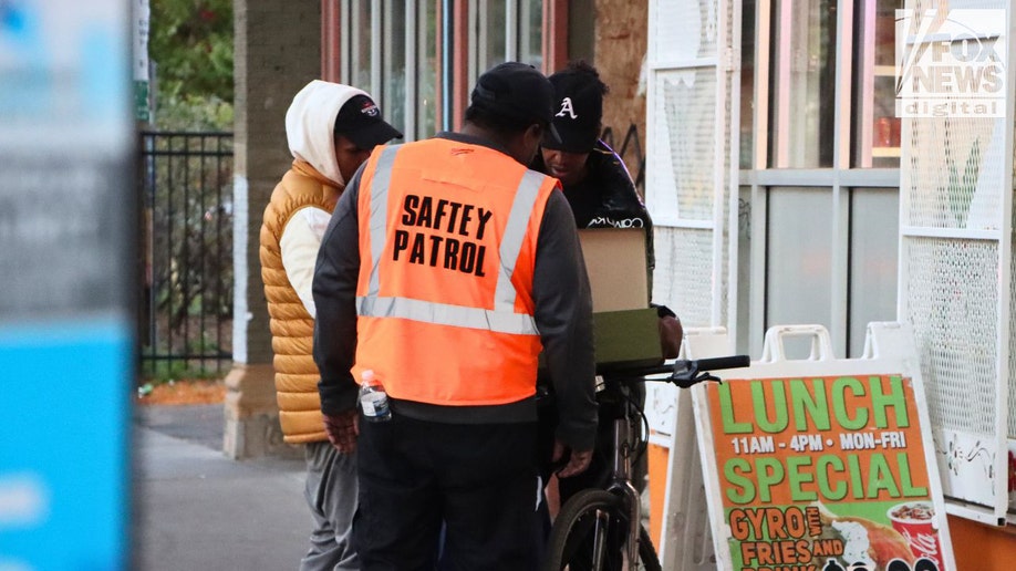 Safety patrol member wearing orange vest speaks with residents in Cedar–Riverside