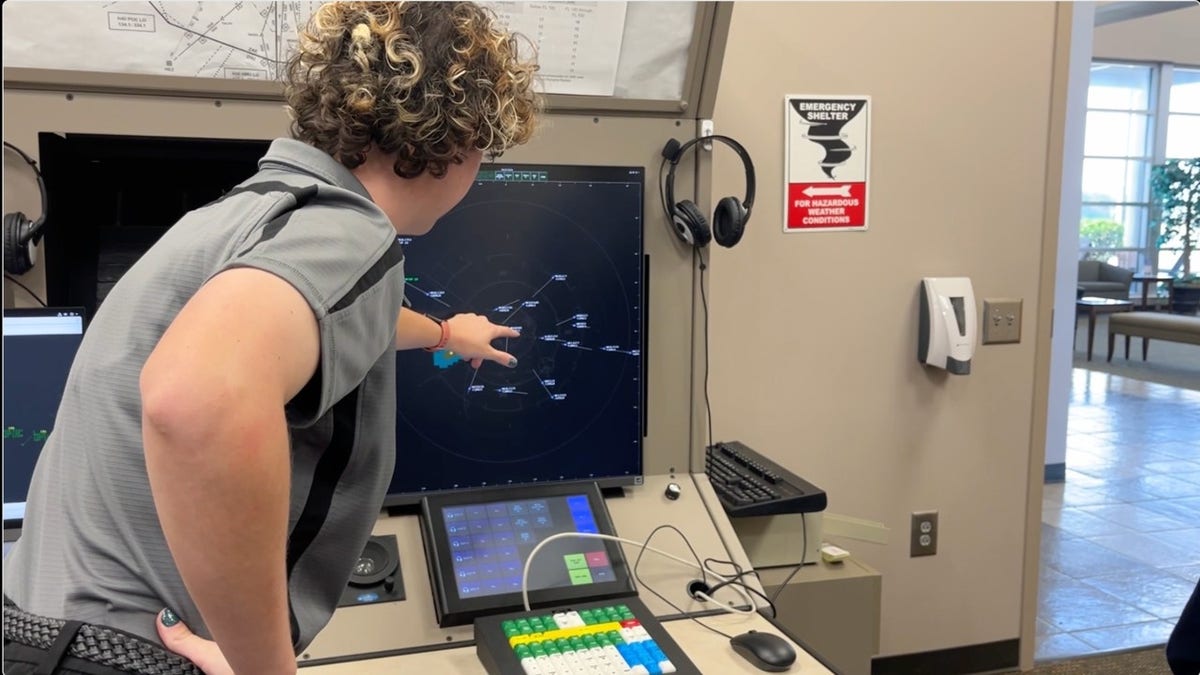 A student points to aircraft targets on a radar screen during an air traffic control lesson.