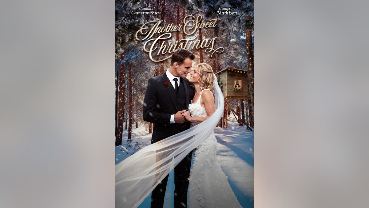 Candace Cameron Bure and Cameron Mathison embrace in a snowy forest, with festive lights and a wooden cabin in the background under the title 