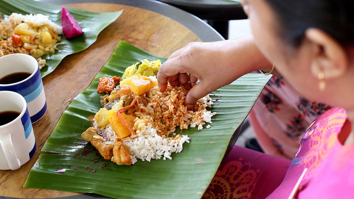 An Asian woman uses her hand to grab rice.