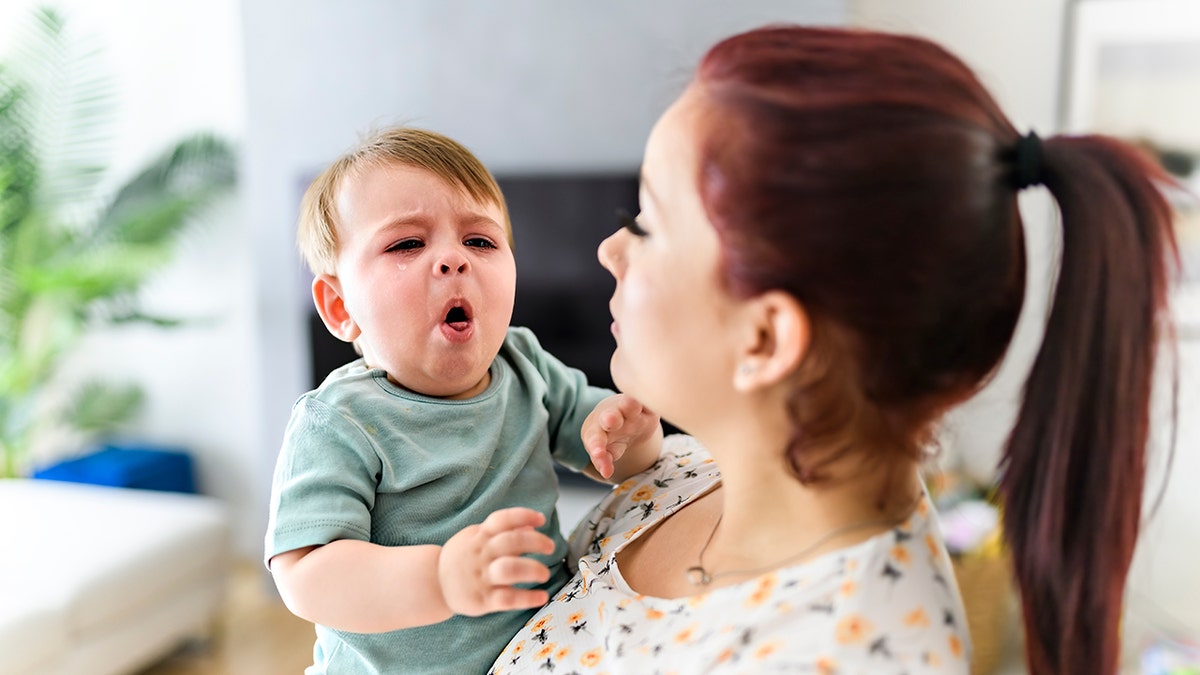 A mother holding child baby on the living room. The baby is coughing