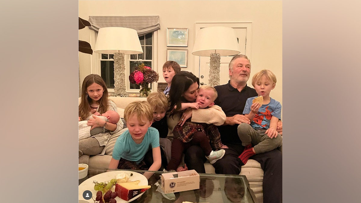 The Baldwin family sits together on a couch in a chaotic Thanksgiving 2022 photo, with several children crying, eating or climbing around the adults.